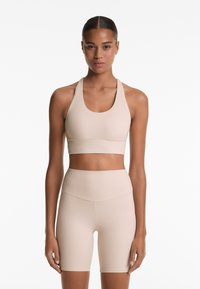 Beige sportbeha met een brede, ronde halslijn en dikke bandjes, gecombineerd met hoge, aansluitende shorts van een gladde, rekbare stof.