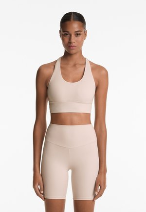 Beige sports bra with a wide, rounded neckline and thick straps, paired with high-waisted, form-fitting shorts made of smooth, stretchy fabric.
