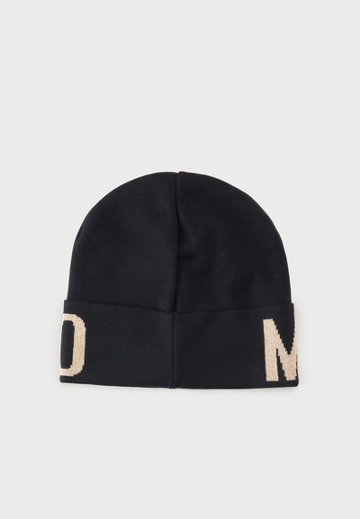 Bonnet en tricot noir avec bord replié comportant de grandes lettres beiges partielles "D" et "M" sur des côtés opposés.