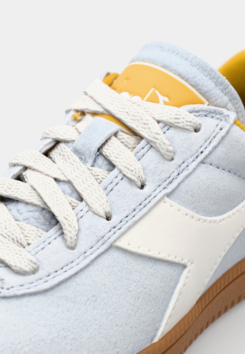 Baskets en suède bleu clair avec des accents blancs, des lacets blancs, une étiquette de logo jaune et une semelle en caoutchouc gomme. Vue rapprochée des détails de conception.