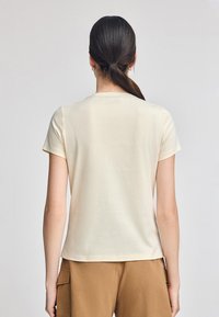 T-shirt a maniche corte color crema realizzato in tessuto morbido, con scollatura rotonda e vestibilità rilassata, visto da dietro.