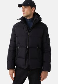 Zwarte quilted jas met capuchon, voorzien van ritszakken, een gladde textuur en een aansluitende pasvorm, gedragen over een donkere turtleneck.