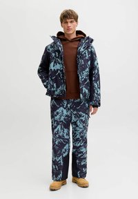 Set di giacca e pantaloni da sci, caratterizzato da una base blu scuro con un motivo di montagne color turchese. La giacca ha un cappuccio, tasche con zip e una texture imbottita.