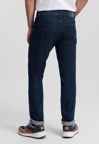 Donkerblauwe denim jeans met een getailleerd ontwerp, voorzien van achterzakken en een omgeslagen zoom. Gdraagd met veelkleurige sportschoenen.