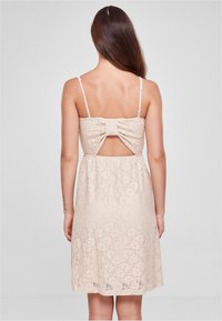 Beige pitsitop dress with spaghetti straps, avatud seljaosa ja paeladetail. Omab lillemustrit kogu kangal ja kellukesekujulist äärt.