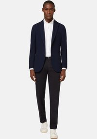 Tamsiai mėlynas bleizeris su notch apykaklėmis, balta marškinėliais ir tamsiomis kelnėmis. Pasižymi dviem priekinėmis kišenėmis ir knopkine uždarymo sistema, derinamas su baltais sportbačiais.