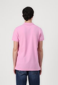 Polo shirt rose à manches courtes, col côtelé et détail d'entoilage au dos. Porté avec un jean bleu déchiré.
