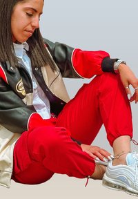 Leather jacket in black and beige with red accents, paired with red joggers and light blue Nike sneakers. Features a white shirt beneath.