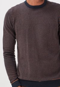 Suéter de punto azul marino con un patrón geométrico en crema. Presenta un cuello redondo y puños y dobladillo acanalados, confeccionado con una tela suave y texturizada.