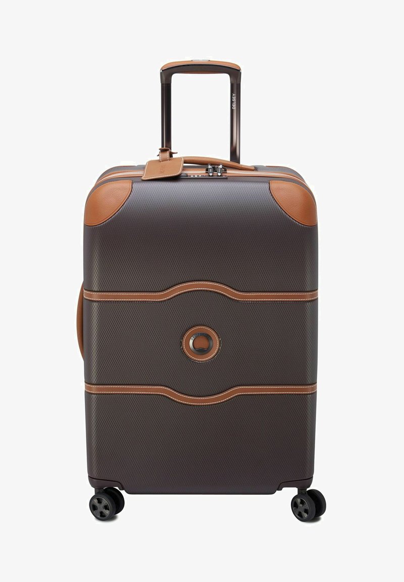 Valise rigide gris foncé avec des accents en cuir beige, texture lisse, poignée télescopique et quatre roues pour une mobilité aisée.