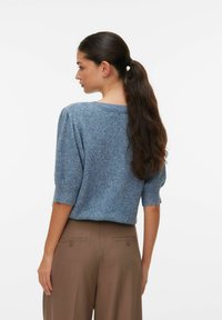 Niebieski sweter dziany z krótkimi rękawami i luźnym krojem, zestawiony z brązowymi, dopasowanymi spodniami. Materiał ma miękką, fakturowaną powierzchnię.