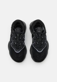 Black athletic shoes with a textured suede upper, mesh detailing, thick sole, and grey accents along the sides and around the laces.
