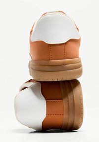 Baskets orange et blanches avec une texture en cuir lisse, dotées d'un talon rembourré et d'une semelle extérieure en caoutchouc avec une adhérence texturée.