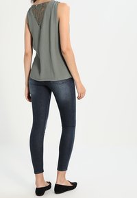 Haut gris sans manches avec un détail en dentelle au dos, associé à un jean skinny bleu foncé et des chaussures plates noires. Design simple, coupe décontractée.