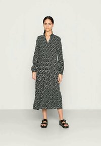 Vestido floral preto com mangas compridas, botão frontal e uma silhueta fluida. Usado com sandálias planas pretas.