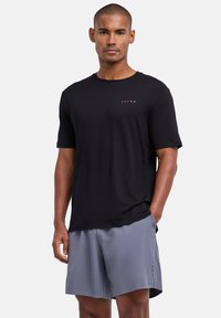 Chemise noire à manches courtes avec le logo rouge "FALKE", associée à un short gris avec de petites touches latérales et une coupe décontractée. Texture de tissu lisse.