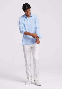 Lichtblauw polohemd met lange mouwen en een knoopsluiting. Gecombineerd met witte slim-fit broeken en witte sneakers.