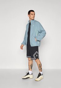 Hele sinine jope lukuga ees ja küljetaskutega, kantud musta särgi ja mustade mustriliste lühikeste pükste kohal. Karamellivärvi tossud mustade detailidega.