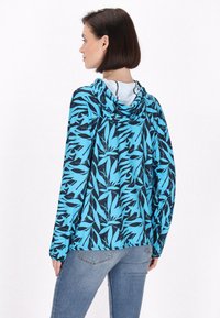 Giacca con cappuccio caratterizzata da un motivo foglia blu e nero, con maniche lunghe e vita elasticizzata, realizzata in materiale leggero e flessibile.