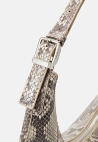 Sac hobo avec un motif serpent dans des tons beige et gris. Doté d'une boucle en métal argenté sur une sangle texturée. Détail zippé présent.