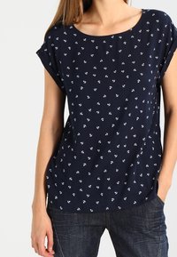 Marinblå kortärmad topp med ett spritt vitt ankarmönster, rund halsringning och avslappnad passform, tillverkad av lättviktsmaterial.