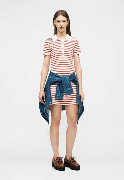 Γυναίκα φορώντας ένα κοντό φόρεμα με κόκκινες και λευκές ρίγες, λευκό γιακά, μια τζιν μπουφάν δεμένη γύρω από τη μέση της και καφέ πλατφόρμες.