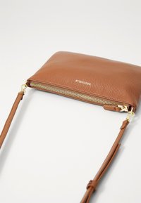 Borsa a tracolla in pelle marrone con texture a granulato, chiusura con zip dorata e strap regolabile. Presenta il nome del brand impresso sul davanti.