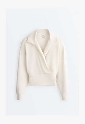 Krémovo sfarbená blúzka s dlhými rukávmi, širokým golierom, zavinovacím predným dielom, nariaseným pásom a priliehavými manžetami.