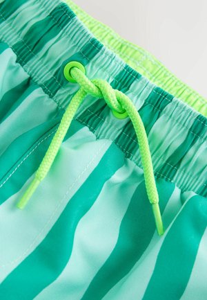 Lähikuva vihreästä ja sinivihreästä raidallisista uimashortseista, joissa on neonvihreä kiristysnauha solmittuna solmuun joustavassa vyötärössä.