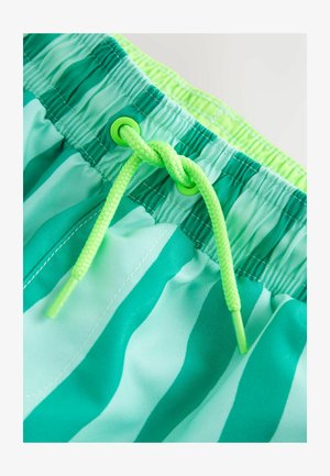 Zbliżenie na zielono-turkusowe kąpielówki w paski z neonowozielonym sznurkiem związanym w węzeł na elastycznym pasie.