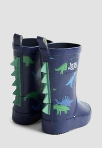 Modré gumové holínky mají vzor zelených dinosaurů a trojúhelníkové zelené akcenty po stranách. Ploché podrážky s texturovaným gripem. Viditelné logo JoJo.