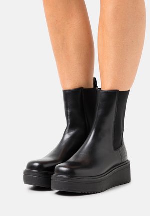 Black leather ankle boots featuring elastic side panels, a chunky platform sole, and a textured back panel. Smooth surface with subtle sheen.