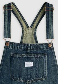 Τζιν φορμάκια με ρυθμιζόμενους ιμάντες που διασταυρώνονται στην πλάτη και μια μεγάλη πίσω τσέπη με ετικέτα Levi Strauss & Co.