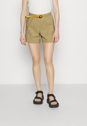 Khaki shorts met een elastische tailleband en een gele verstelbare riem; gecombineerd met zwarte sandalen met een plateauzool en banden.