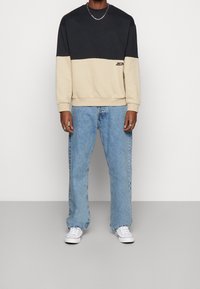 Felpa a blocchi di colore in navy e beige, in misto cotone, con polsini a costine. Abbinata a jeans a gamba dritta blu chiaro e sneakers bianche.