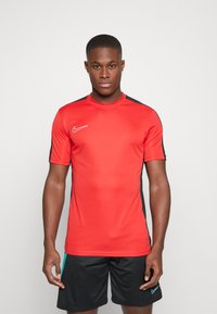 Punane spordisärk lühikeste varrukatega, ümmargune kaelus, mustad küljeakatused ja valge Nike logo rinnal. Kandetuks mustade lühikeste pükstega.