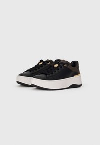 Sorte lavtop sneakers med tykke hvite såler, svarte snøringer og brune mønstrede hældetaljer med gulllogo.