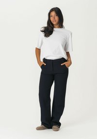 Black tailored pants with a smooth texture and side pockets, paired with a loose-fitting white t-shirt. Casual shoes complete the outfit.