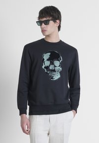 Sweatshirt noir avec un grand motif de crâne en teintes de turquoise et de gris. Texture douce avec un col rond classique et des poignets côtelés.