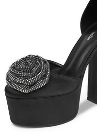 Černé platformové sandály na vysokém podpatku s tlustým blokovým podpatkem a velkou černou růží zdobenou malými stříbrnými rhinestonami na špičce.