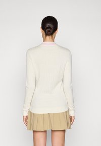 Pull en crème à côtes avec un col rond rose, des manches longues et un design ajusté, associé à une jupe plissée beige.