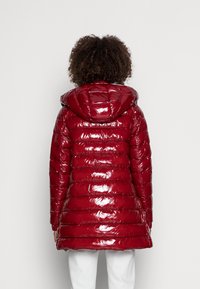 Red, glossy puffer jacket with a hood, featuring horizontal quilted sections and a mid-length design. Smooth texture and modern silhouette.