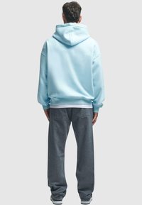 Light blue pullover hoodie with a hood and long sleeves, paired with gray, loose-fitting jeans. Fabric texture appears soft and comfortable.