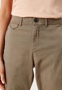 Primo piano di una persona che indossa pantaloni beige con una vita ripiegata e una camicia rosa chiaro infilata dentro.