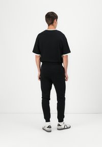 Schwarzes T-Shirt mit weißem Saum, kombiniert mit schwarzen Jogginghosen. Die Jogginghosen haben einen elastischen Bund und Taschen. Schlichtes, lässiges Design.