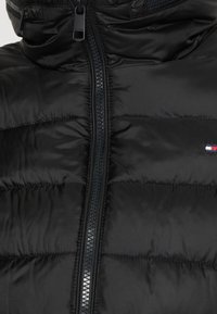 Czarna kurtka puchowa z wysokim kołnierzem, zamkiem błyskawicznym z przodu oraz subtelnym poziomym przeszyciem. Zawiera małe logo po lewej stronie.