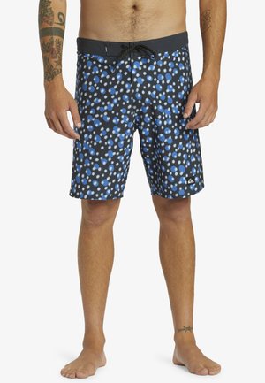 Black swim shorts with a blue and white polka dot pattern, elastic waistband with drawstring, and a small logo on the lower left side.