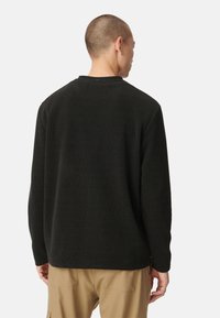 Czarny prążkowany longsleeve z okrągłym dekoltem, charakteryzujący się teksturowanym materiałem i luźnym krojem, zestawiony z beżowymi spodniami.