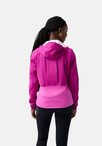 Roze gebreide jas met een contrasterend laag paneel. Soepele textuur, lichte stof, elastische manchetten en een achterventilatie voor ademend vermogen.