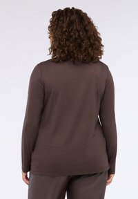 Camicia a maniche lunghe marrone con una texture liscia, caratterizzata da una vestibilità comoda e fessure laterali. Il design presenta un orlo posteriore arrotondato e dettagli di cucitura sottili.